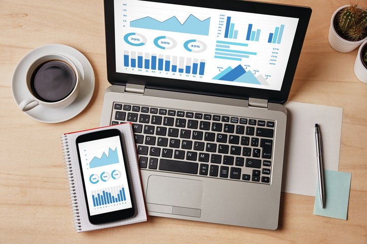 computer and phone on a desk displaying charts and graphs