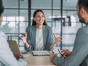 A smiling female accountant sits at an office table with two clients.