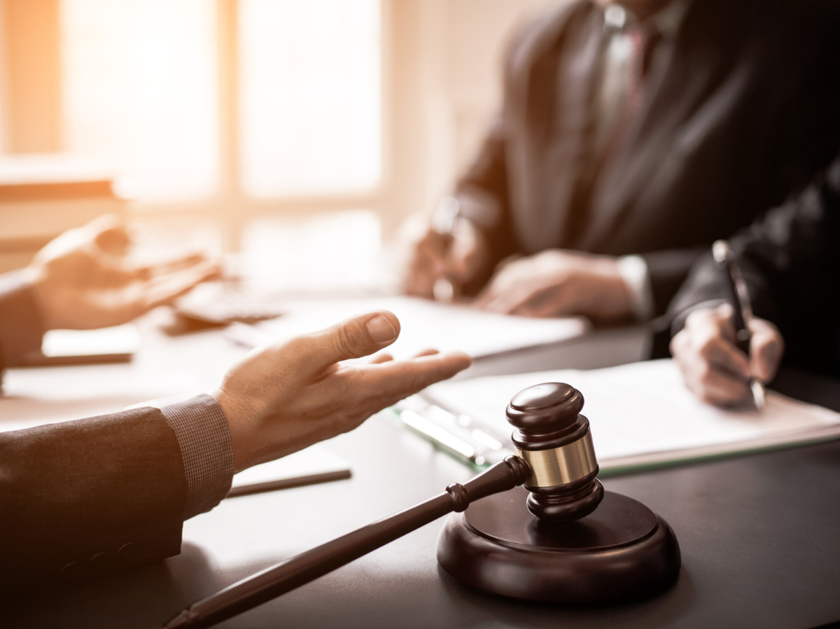 Business people sit around a table with documents and a wooden gavel.